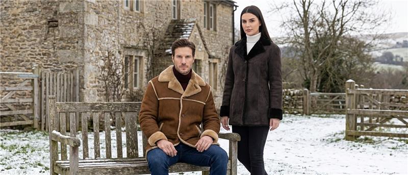 Man and woman wearing shearling coats in a snowy countryside setting.